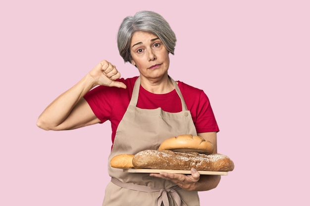 Fornaio caucasico di mezza età con pane che mostra un gesto di disgusto pollice verso il basso concetto di disaccordo