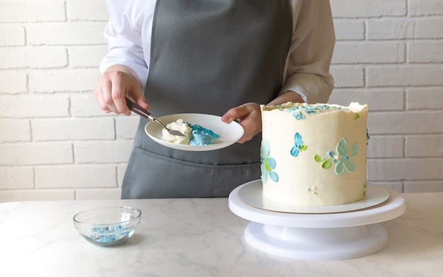 Fornaio femminile che decora con una gustosa torta alla crema sul tavolo.