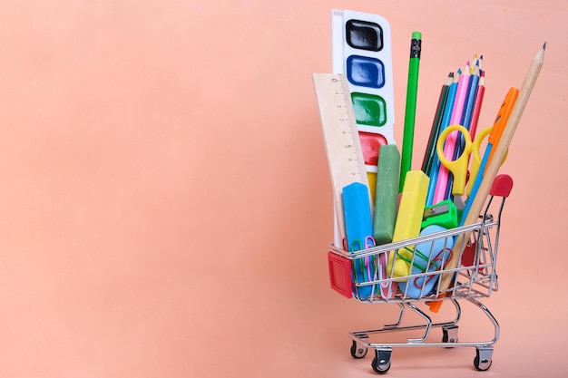 Forniture scolastiche e cancelleria in un carrello sfondo rosaPreparare il bambino per l'anno scolastico