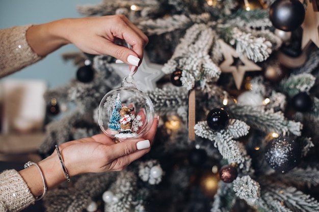 Foro ritagliato delle mani della signora che tengono un bellissimo giocattolo di cervo vicino all'albero di Natale. Concetto di capodanno