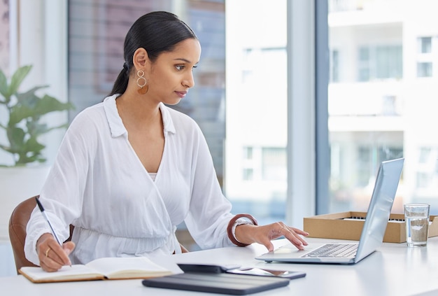 Forse non vendo Foto di una donna d'affari che usa un laptop in un ufficio moderno e prende appunti su un taccuino