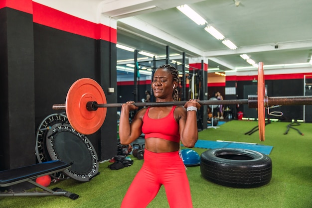 Forte atleta nero in una palestra che fa esercizi con bilanciere e sollevamento pesi per rafforzare spalle e bicipiti che mostrano molto sforzo e in abbigliamento sportivo rosso