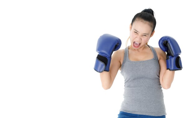 Forte e determinata giovane donna asiatica con guanti da boxe blu che colpiscono e perforano aria su sfondo bianco