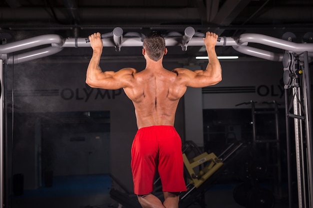 Forte giovane che fa pull up esercizio sulla barra orizzontale in palestra