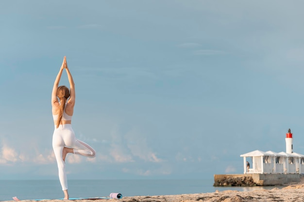 Forte giovane donna fitness che pratica yoga albero pongono all'aperto sullo sfondo del mare Vista posteriore Yoga in spiaggia