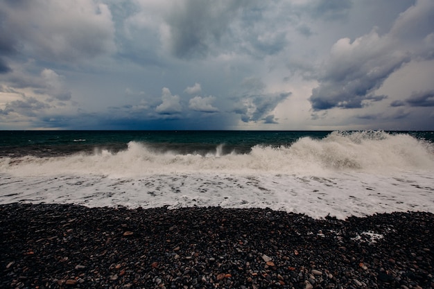 Forte mareggiata. Le onde bianche rotolano su una spiaggia di pietra. Cumuli nel cielo.