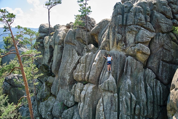 Forte scalatore del bambino che scala la parete ripida della montagna rocciosa. Giovane ragazzo che supera un percorso difficile. Impegnarsi nel concetto di hobby di sport estremi.