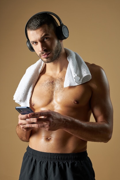 Forte uomo adorabile con corpo muscoloso in cuffia utilizzando smartphone in camera al chiuso