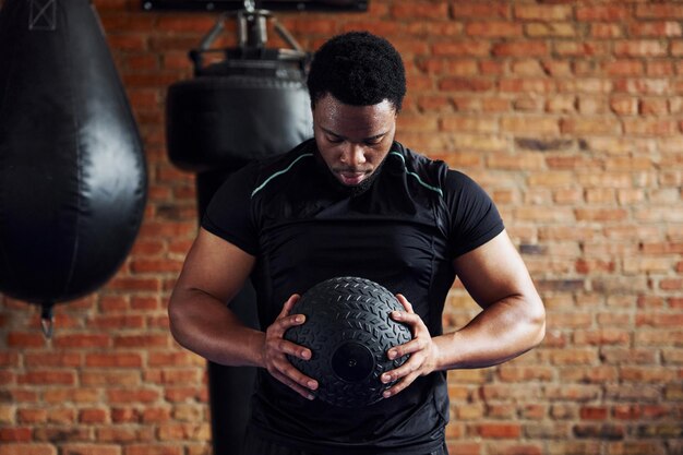 Forte uomo afroamericano in abiti sportivi in palestra e con la palla in mano