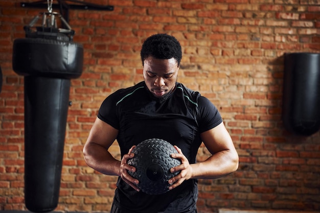 Forte uomo afroamericano in abiti sportivi in palestra e con la palla in mano