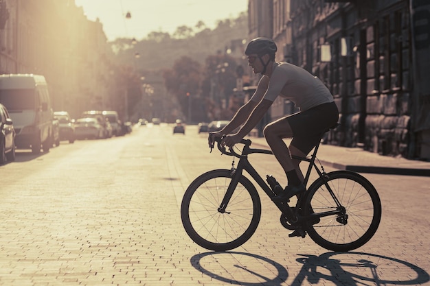 Forte uomo caucasico con casco di sicurezza e occhiali che praticano il ciclismo all'aperto Luce solare mattutina su una strada vuota della città Allenamento regolare durante l'estate