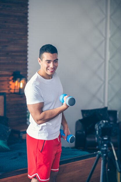 Forte uomo dai capelli scuri in pantaloncini rossi sorridendo piacevolmente lavorando con il manubrio