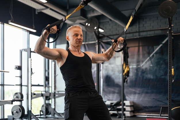 Forte uomo di mezza età che fa flessioni con TRX in palestra