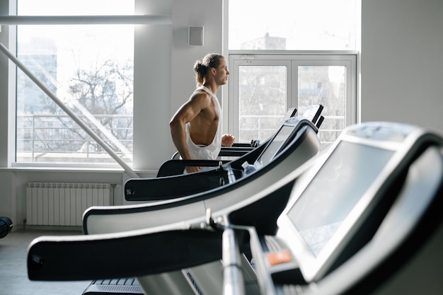 Forte uomo muscoloso che corre sul tapis roulant nella moderna palestra sportiva