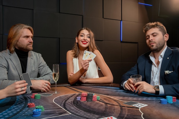 Fortunata ed elegante giovane ragazza dai capelli castani felice con il successo del gioco del poker seduto al tavolo, dimostrando un set di carte vincenti da una coppia di assi ad avversari delusi. La fortuna sorrise