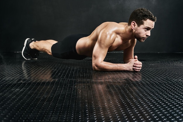 Forza di base Foto in studio di un giovane uomo senza maglietta che plana su uno sfondo scuro