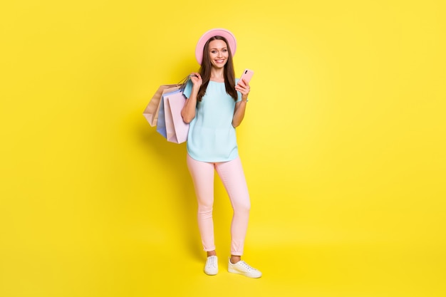 Foto a figura intera del cliente del centro commerciale della ragazza che legge le notizie fuori dalle vendite usa lo smartphone indossa una t-shirt blu rosa pantaloni pantaloni cappello da sole berretto isolato su uno sfondo di colore brillante brillante