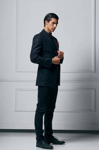 Foto a figura intera di un giovane fiducioso elegante in abito nero, guardando di profilo, su sfondo bianco.