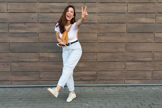 Foto a figura intera di una bella giovane donna bruna felice che indossa abiti casual e ascolta