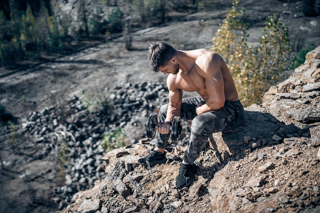 Foto a grandezza naturale di un ragazzo atletico in posa con roccia in una cava Ripresa all'aperto Bodybuilder Cava sfondo Primo piano Manubri in mano