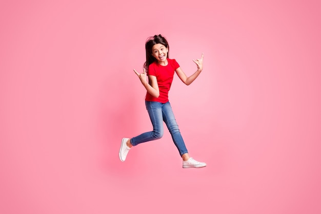 Foto a grandezza naturale di una ragazza pazza che salta mostra un simbolo cornuto indossa una maglietta rossa in denim isolato su uno sfondo di colore pastello