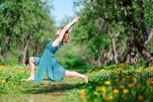 Foto a lato della giovane donna con le braccia alzate in abito lungo verde che fa yoga nella foresta il giorno d'estate