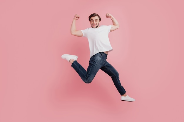 Foto a tutta lunghezza di un giovane uomo felice sorridente eccitato e positivo si diverte a gioire della vittoria mostra i muscoli isolati su uno sfondo di colore rosa