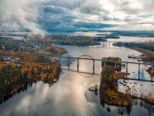 Foto aerea del vecchio ponte sospeso ferroviario sopra il fiume. Paesaggio autunnale con la natura del nord. Alberi con foglie gialle e arancioni sullo sfondo. Cielo nuvoloso. concetto di trasporto.