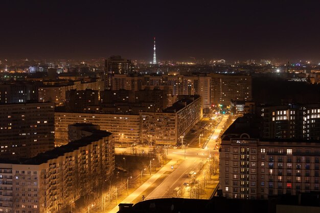 Foto aerea notturna della strada con lanterne accese e alti edifici residenziali. Torre televisiva illuminata sullo sfondo. Grande concetto di vita della città.