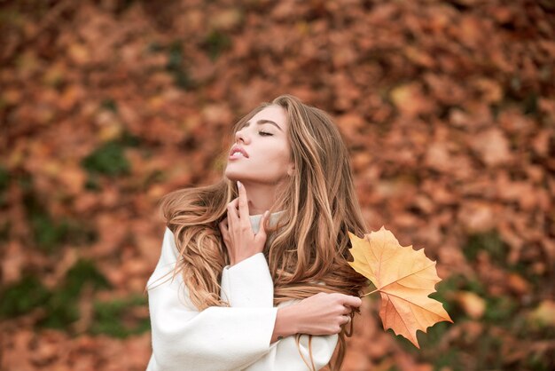Foto all'aperto della donna di autunno della giovane donna sulle foglie foto di stile di vita atmosferica all'aperto del giovane bea