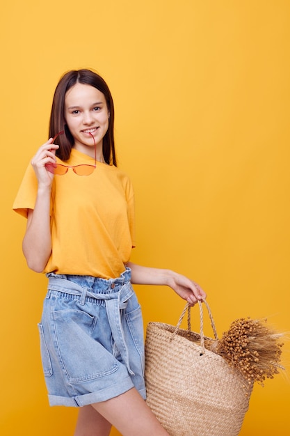 Foto bella ragazza borsa da spiaggia moda in maglietta gialla pantaloncini di jeans sfondo giallo