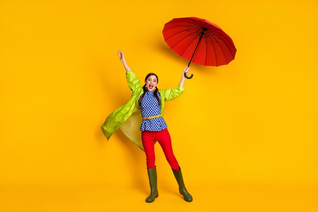 Foto completa del corpo di una ragazza energica e eccitata che tiene un parasole rosso aria che soffia vento indossa un bell'abito scarpe di gomma isolate su uno sfondo di colore brillante e brillante