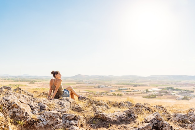 Foto con copia spazio di una donna seduta su una collina che domina i campi della pianura in una giornata di sole e vento a Toledo, Spagna