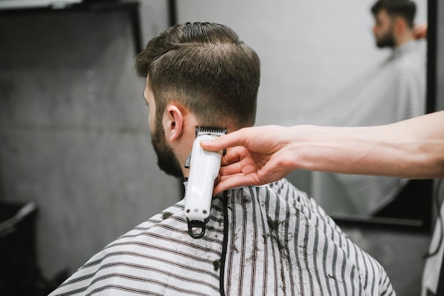 foto concerto barbiere Parrucchiere a mano con clipper taglia i capelli di un uomo adulto barbuto con i capelli scuri