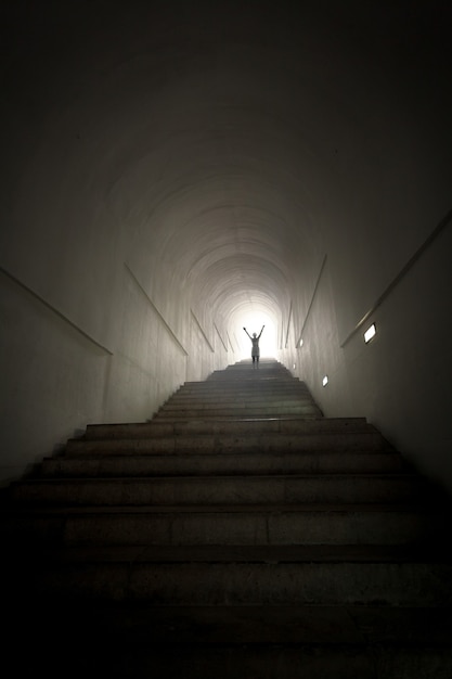 Foto concettuale della persona in piedi alla fine del tunnel al raggio di luce con le mani alzate