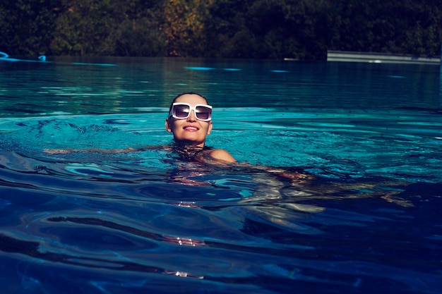Foto d'epoca di una donna in costume da bagno nero e occhiali da sole bianchi che nuotano in piscina