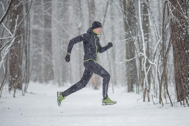 Foto dal lato dell'uomo in abbigliamento sportivo in esecuzione in inverno