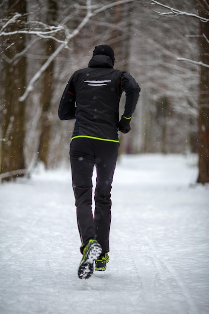 Foto dal retro dell'atleta in esecuzione tra gli alberi nella foresta invernale