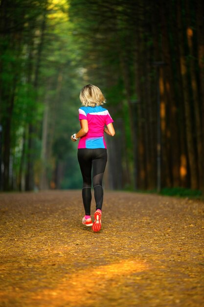 Foto dal retro della donna sportiva che corre attraverso il parco tra gli alberi la mattina d'estate.