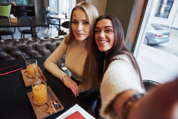 Foto dal telefono della ragazza. Le giovani amiche prendono selfie nel ristorante con due drink gialli sul tavolo