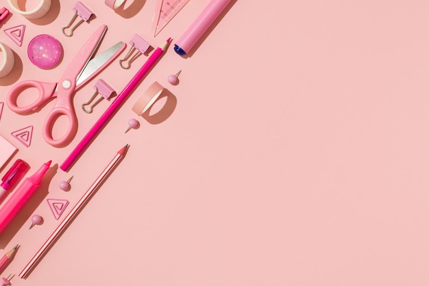 Foto dall'alto della cancelleria rosa ordinata nastri adesivi puntine da disegno clip per raccoglitori forbici matite pennarelli e righello su sfondo rosa pastello isolato con spazio vuoto