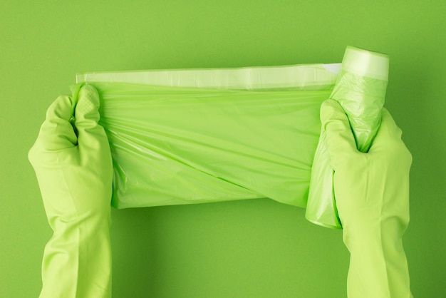 Foto dall'alto delle mani in guanti di gomma verdi che aprono nuovi sacchi della spazzatura su sfondo verde isolato con copyspace