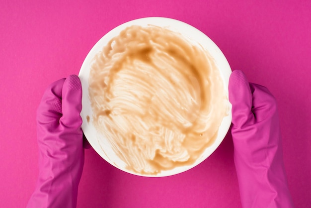 Foto dall'alto di mani in guanti di gomma rosa che tengono piatto sporco su sfondo rosa isolato