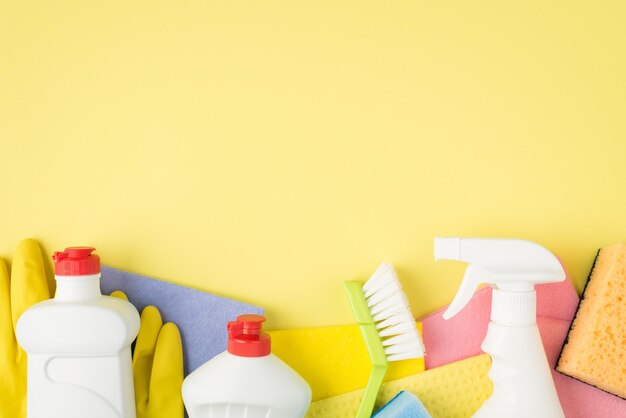 Foto dall'alto di stracci di viscosa multicolori guanti di gomma spugne spray per pennelli e bottiglie di detersivo in gel su sfondo giallo isolato con copyspace