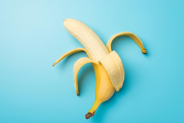 Foto dall'alto di una banana matura sbucciata al centro su sfondo blu pastello isolato