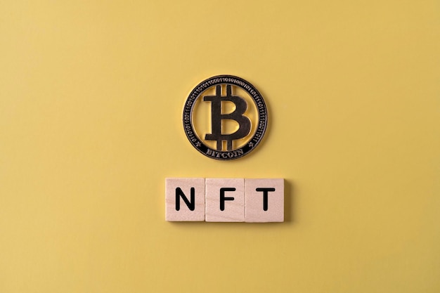 Foto dall'alto sulla parola NFT con moneta di criptovaluta blockchain Bitcoin su sfondo giallo