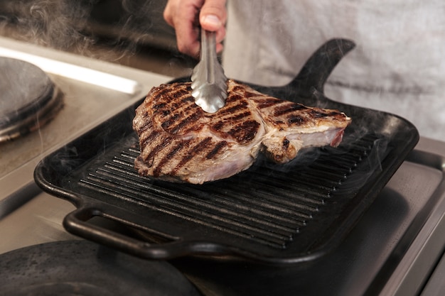 Foto del capo uomo adulto in uniforme bianca, grigliare carne in cucina nel ristorante