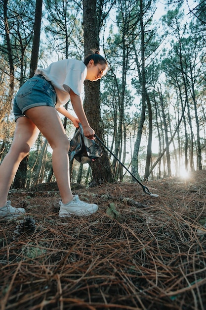 Foto del lato della ragazza che raccoglie immondizia nella borsa sulla foresta durante un tramontoInquinamento ambientale dei rifiutiNatura pulizia volontario ecologia concetto verde