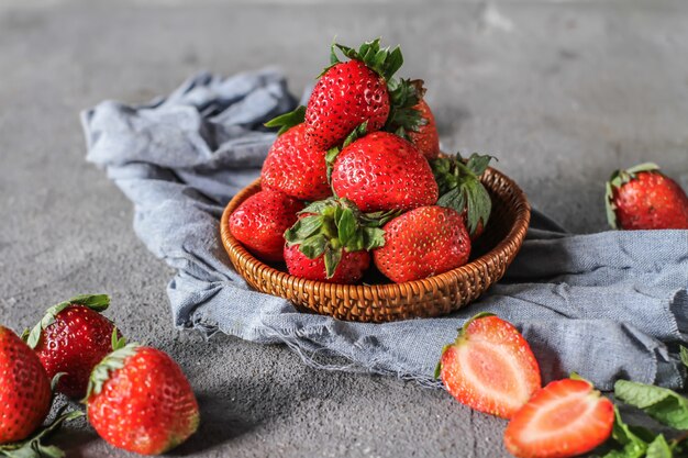 Foto del mucchio delle fragole fresche nella ciotola su fondo grigio rustico. Un mazzo di fragole mature in una ciotola di legno sul tavolo. Copia spazio. Sana frutta fresca. Cibo organico. Cestino di legno