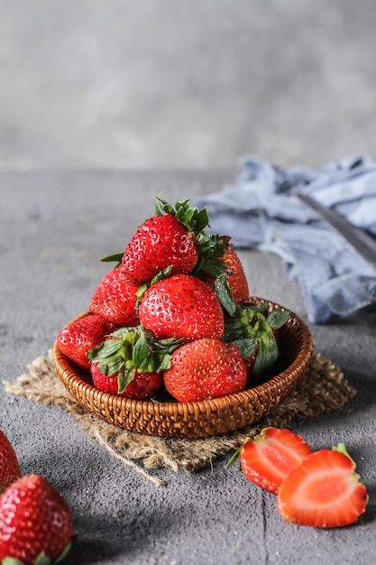 Foto del mucchio delle fragole fresche nella ciotola su fondo grigio rustico. Un mazzo di fragole mature in una ciotola di legno sul tavolo. Copia spazio. Sana frutta fresca. Cibo organico. Cestino di legno